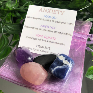 A selection of crystal crystal tumble stones including Sodalite, Amethyst, Rose Quartz and Hematite. A pink/purple organza bag. An information card with Anxiety at the top then below is a list of the crystals with a description of their healing properties.